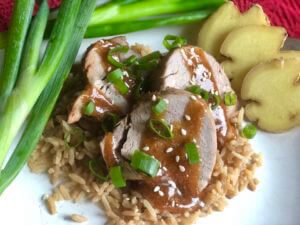 Pork Tenderloin with Honey Soy Sauce, sprinkled with green onions and sesame seeds on a bed of brown rice.