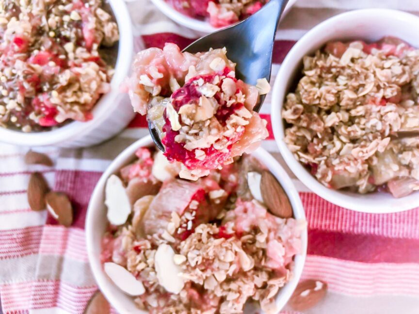 SPOON OF HEALTHY STRAWBERRY RHUBARB CRUMBLE WITH 3 BOWLS IN THE BACKGROUND